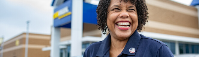 Four CarMax associates sit in a row, wearing headphones in an office. The one in front is in focus, smiling and looking off to the right.